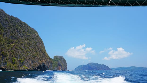 Waves from the engines of a high-speed boat. Rear view. Blue sky, white cloud and far island. White foam from waves. Floating in the ocean.