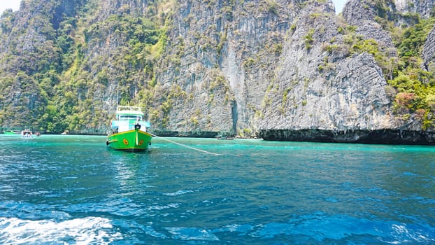 Blue water, green hills and steep rocks. The boat sails near the island. Boat with tourists in the Bay. Steep cliffs and caves. Group of tourists on the boat. Sea excursion. Water gradient.