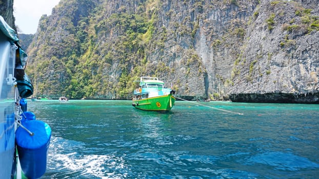 Blue water, green hills and steep rocks. The boat sails near the island. Boat with tourists in the Bay. Steep cliffs and caves. Group of tourists on the boat. Sea excursion. Water gradient.