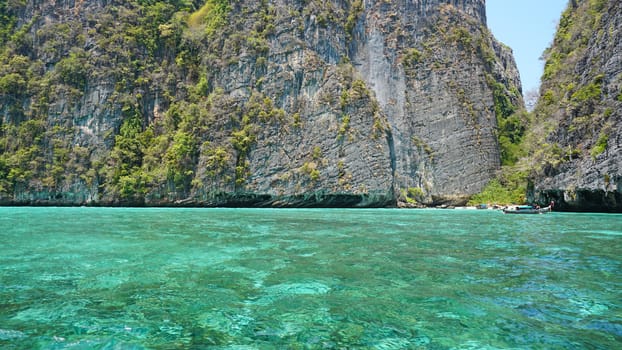 Blue water, green hills and steep rocks. The boat sails near the island. Boat with tourists in the Bay. Steep cliffs and caves. Group of tourists on the boat. Sea excursion. Water gradient.