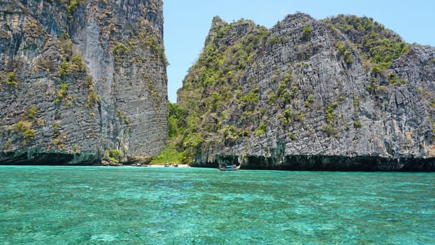 Blue water, green hills and steep rocks. The boat sails near the island. Boat with tourists in the Bay. Steep cliffs and caves. Group of tourists on the boat. Sea excursion. Water gradient.