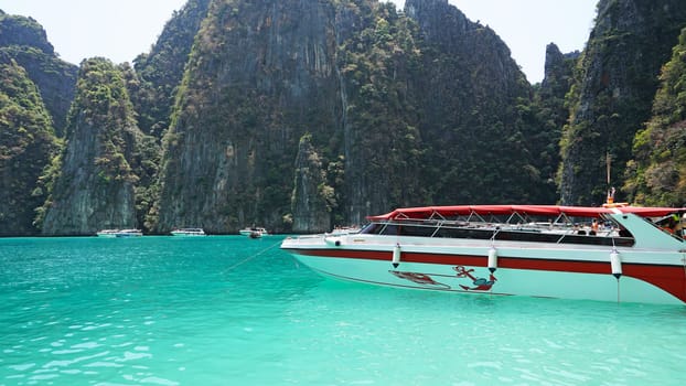 Blue water, green hills and steep rocks. The boat sails near the island. Boat with tourists in the Bay. Steep cliffs and caves. Group of tourists on the boat. Sea excursion. Water gradient.