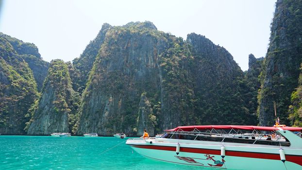 Blue water, green hills and steep rocks. The boat sails near the island. Boat with tourists in the Bay. Steep cliffs and caves. Group of tourists on the boat. Sea excursion. Water gradient.