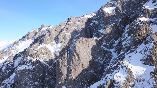 Huge rocks covered with snow. Dangerous terrain. High mountains, cliffs, and large rocks. Shadow from the sun's rays. Top and side view from the drone. An epic place. The Mountains Of Almaty.