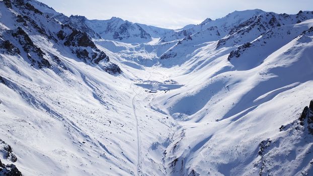 High snowy mountains, spruce trees grow in places. Huge rocks and cliffs, gorges where there may be an avalanche. Top view from a drone. Sunny day, shadows from the mountains fall on the snow. Almaty