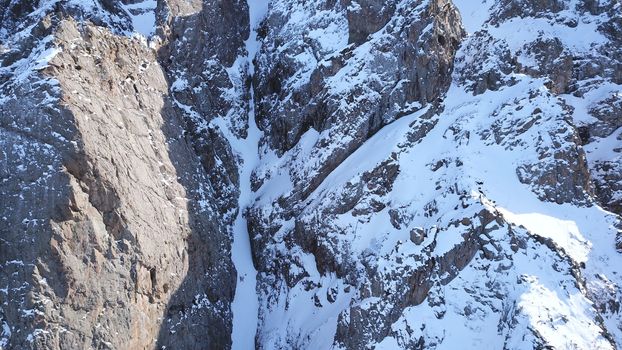 Huge rocks covered with snow. Dangerous terrain. High mountains, cliffs, and large rocks. Shadow from the sun's rays. Top and side view from the drone. An epic place. The Mountains Of Almaty.