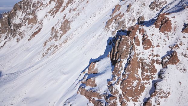 Huge rocks covered with snow. Dangerous terrain. High mountains, cliffs, and large rocks. Shadow from the sun's rays. Top and side view from the drone. An epic place. The Mountains Of Almaty.