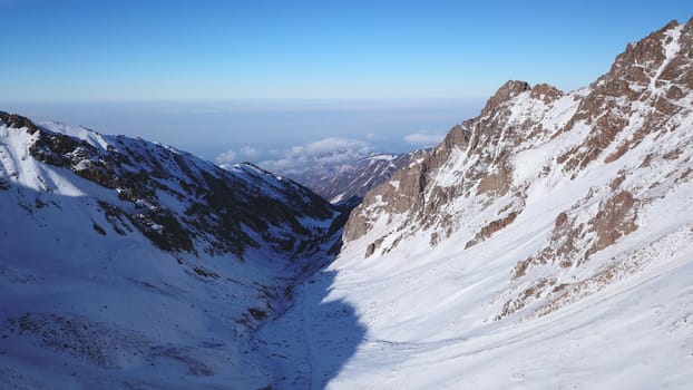 Snow mountain peaks with rocks. View from drone. In places, you can see glaciers, large rocks and rocks. Huge drifts of snow covered mountains. Dangerous place. Blue sky and sun. Shadow of the peaks.