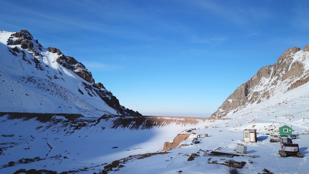 Snow mountain peaks with rocks. View from drone. In places, you can see glaciers, large rocks and rocks. Huge drifts of snow covered mountains. Dangerous place. Blue sky and sun. Shadow of the peaks.