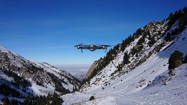 DJI Mavic Pro in the air in the winter gorge. A professional quadcopter takes pictures of nature. Mountainous terrain, winter, lots of snow. Pine trees grow on the rocks. The Mountains Of Almaty.