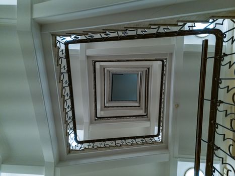 Upward view to old square spiral staircase with metal railings