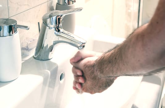 a man washing his hands in a white ceramic sink. Personal care and cleaning. Chrome tap and soap container