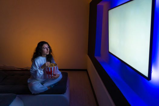 person watches a movie sitting on the couch with a bucket of popcorn.