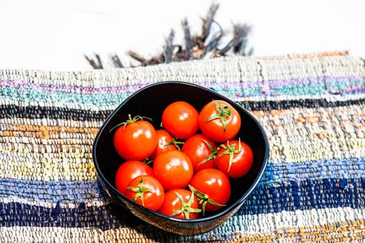Detail of ripe cherry tomatoes in small black bowl on a rustic napkin. Ingredients and food concept