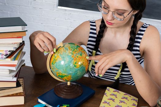 The schoolgirl sits in a desk on the background of a school blackboard. Dark long hair tied in two braids. The glasses are on the nose.