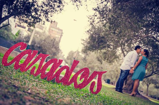 Romantic couple kisses at sunset in the forest full of trees and some letters that say married 