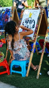 Cute little girl with braids sitting painting outdoors in a park