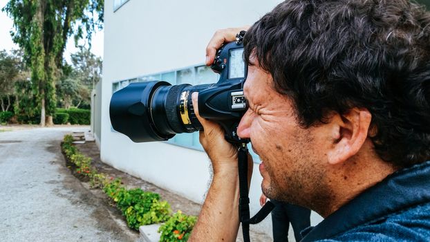 Portrait of a photographer covering his face with the camera. Observing through the viewer