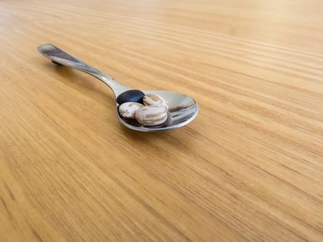 Steel spoon with carioca beans and black beans, on wooden table.
