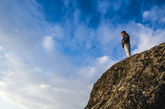 Young man with sunglasses at the foot of a cliff looking at the horizon