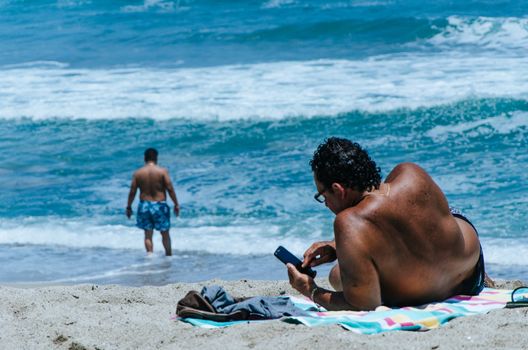 Man resting, relaxing on the beach watching his cellphone