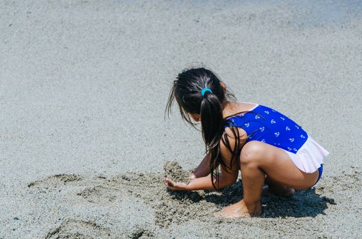 Hands of little girl play with sand on beach