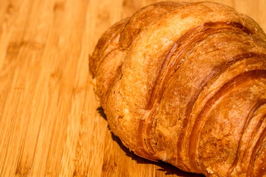 Detail of fresh croissant on wooden table. Food and breakfast concept. Close up photo of French buttery croissant