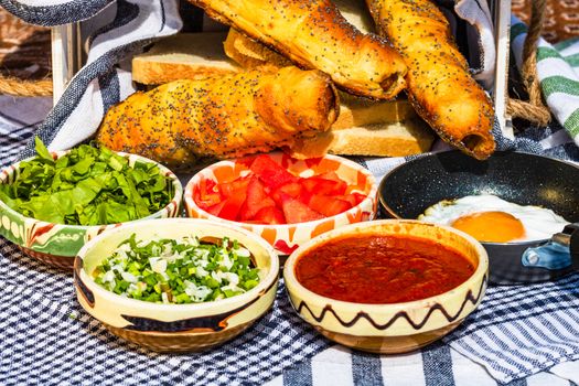 Rustic composition with sausages rolls and different bowls with sauce and chopped vegetables ( tomatoes, green lettuce, green onion, green garlic)