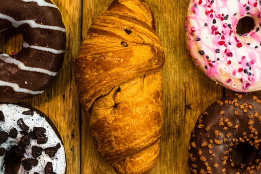 Colorful donuts on wooden table. Sweet icing sugar food with glazed sprinkles, doughnut with chocolate frosting. Top view with copy space