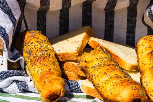 Sausages baked in dough sprinkled with salt and poppy seeds in a rustic composition. Sausages rolls, delicious homemade pastries.