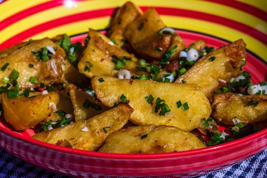 Close up with selective focus of fried potatoes with green onion, green garlic and spices in a colorful plate.