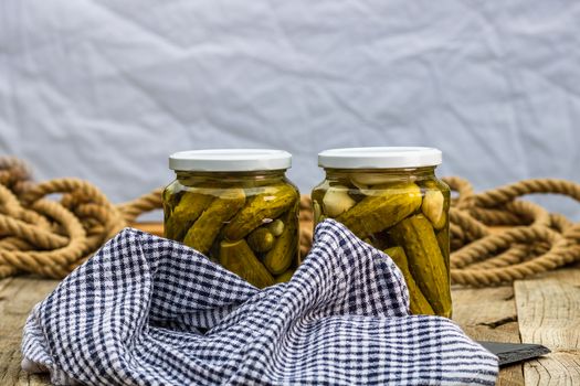 Glass jars with pickled red bell peppers and pickled cucumbers (pickles) isolated. Jars with variety of pickled vegetables. Preserved food concept in a rustic composition.