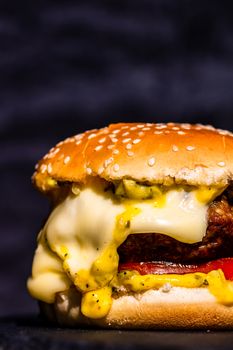 Detail of beef cheeseburger with melted cheese isolated on black background.