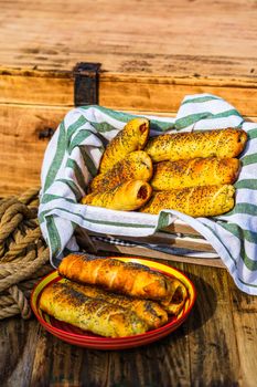 Sausages baked in dough sprinkled with salt and poppy seeds in a rustic composition. Sausages rolls, delicious homemade pastries.