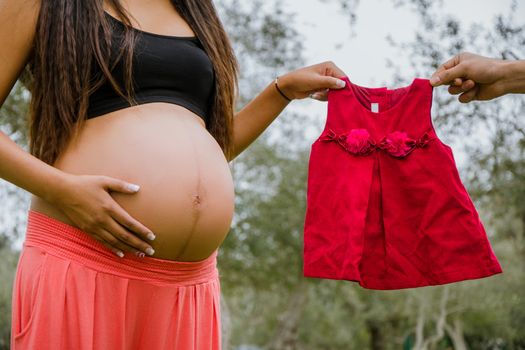 Red dress next to the belly of a pregnant woman, with park background