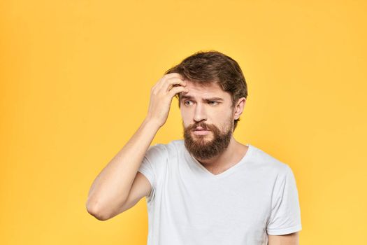 Bearded man in a white T-shirt gestures with his hands emotions studio yellow background. High quality photo