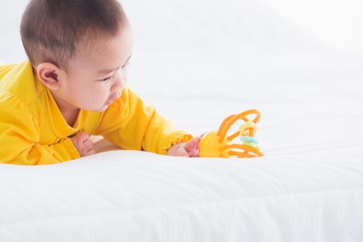 Portrait of beautiful young Asian newborn little baby prone on the bed at home, Happy baby smile wears a yellow shirt relaxing in the room, Family morning at home