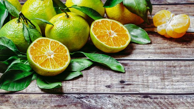 Green mandarines on old wooden background. Fresh ripe half, whole and peeled green tangerines with leaves, top view or flat lay. Copy space for text or design.