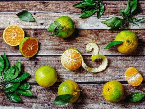 Green mandarines on old wooden background. Fresh ripe half, whole and peeled green tangerines with leaves, top view or flat lay