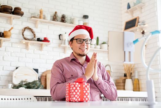Christmas online greetings. Happy young man in santa hat greeting his friends in video chat or call on tablet clapping his hands