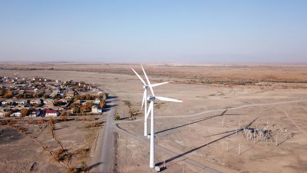 Windmills in the steppe. Near a small town. Alternative, clean energy. Top view from the drone on the long blades. The propeller spins, shadows fall to the ground. Orange sand, near a farm. Kazakhstan