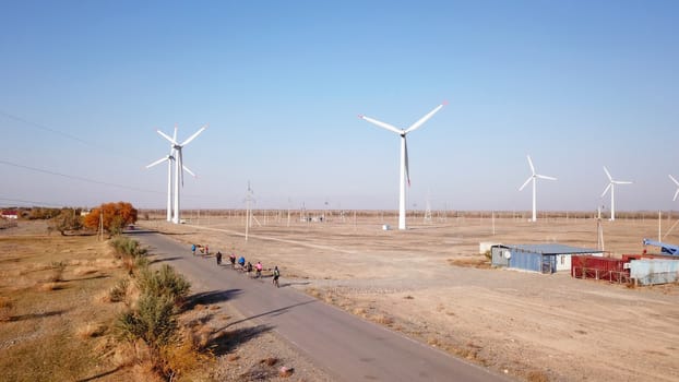 Cyclists ride along the road with a view of the windmills. Alternative, clean energy is produced. Ride on ecological transport. Travel on the road by Bicycle. Steppe. Top view from a drone. Kazakhstan