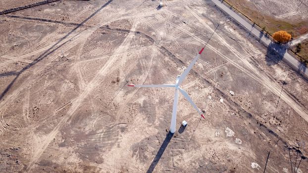 Windmills in the steppe. Near a small town. Alternative, clean energy. Top view from the drone on the long blades. The propeller spins, shadows fall to the ground. Orange sand, near a farm. Kazakhstan