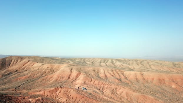 Colored hills of the gorge in the desert. Top view from drone of the red-orange-yellow hills. Cut in different layers, like epochs. Clay of the mountain. Low dry bushes, cracks, blue sky. Kazakhstan.