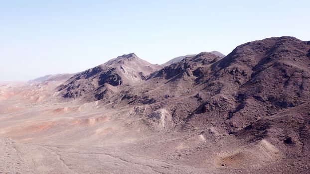 Stony hills of dark color in the steppe. Top view from the drone of rocks, dry bushes, road and gorge. Bright Sunny day and blue sky. A desolate area, the land dried up. Steppes Of Kazakhstan.