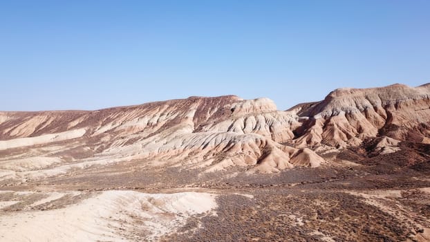 Colored hills of the gorge in the desert. Top view from drone of the red-orange-yellow hills. Cut in different layers, like epochs. Clay of the mountain. Low dry bushes, cracks, blue sky. Kazakhstan.