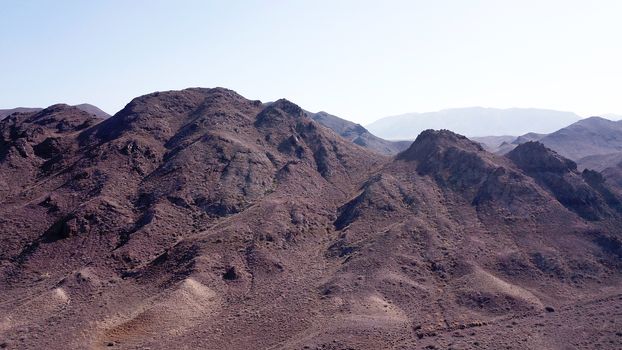 Stony hills of dark color in the steppe. Top view from the drone of rocks, dry bushes, road and gorge. Bright Sunny day and blue sky. A desolate area, the land dried up. Steppes Of Kazakhstan.