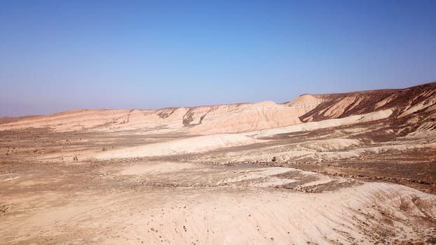 Colored hills of the gorge in the desert. Top view from drone of the red-orange-yellow hills. Cut in different layers, like epochs. Clay of the mountain. Low dry bushes, cracks, blue sky. Kazakhstan.