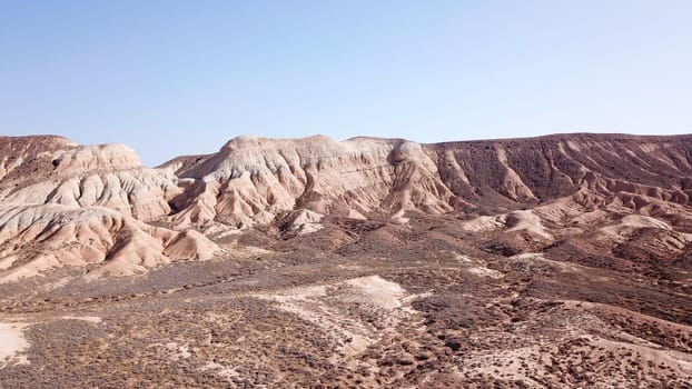 Colored hills of the gorge in the desert. Top view from drone of the red-orange-yellow hills. Cut in different layers, like epochs. Clay of the mountain. Low dry bushes, cracks, blue sky. Kazakhstan.