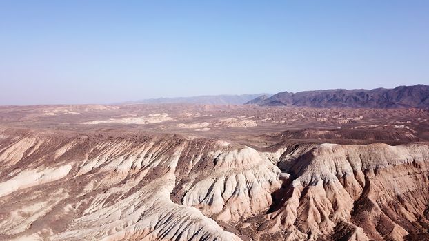 Colored hills of the gorge in the desert. Top view from drone of the red-orange-yellow hills. Cut in different layers, like epochs. Clay of the mountain. Low dry bushes, cracks, blue sky. Kazakhstan.